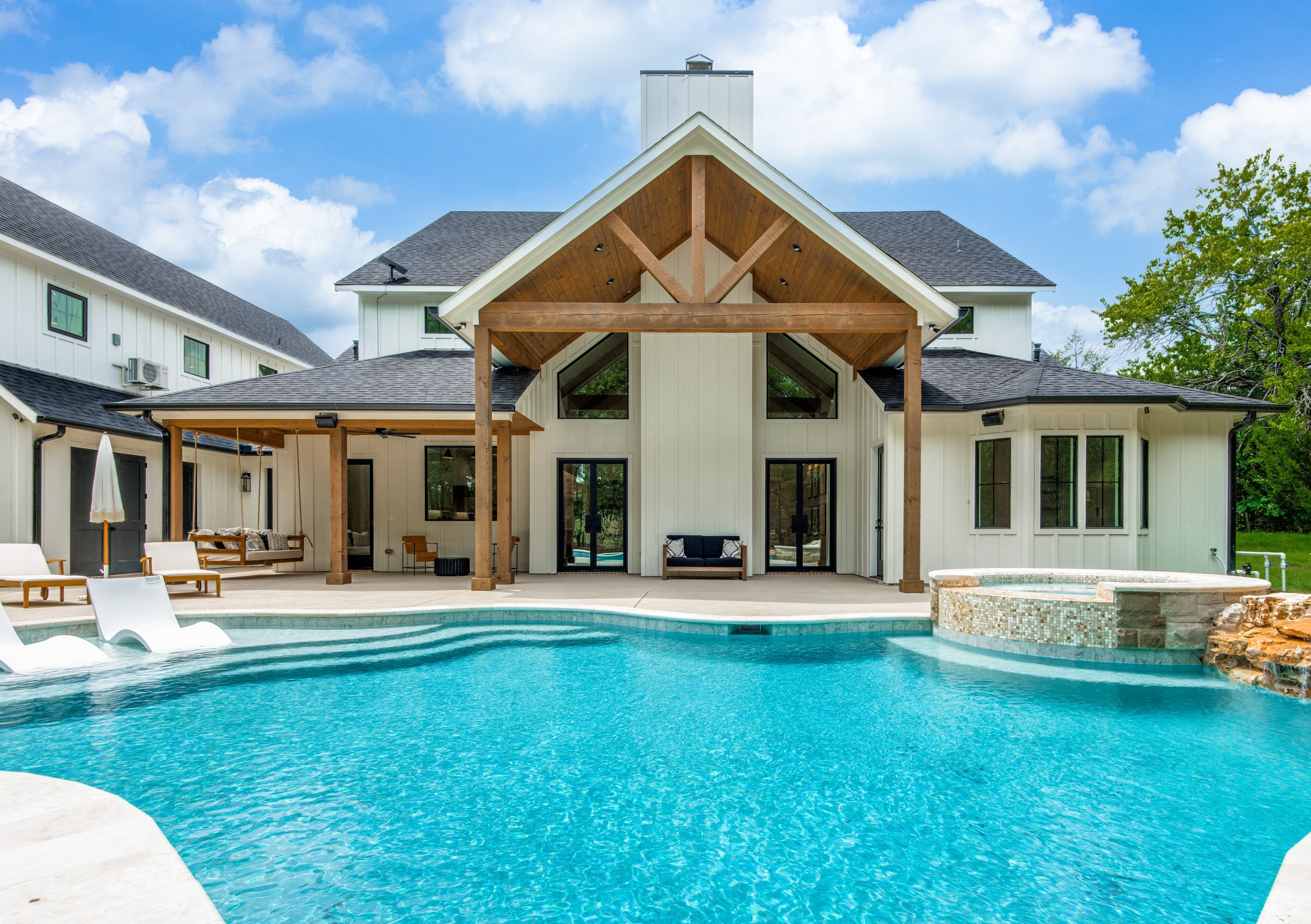 OKC custom home design featuring a vaulted cedar porch, black-frame windows, and resort-style pool and spa